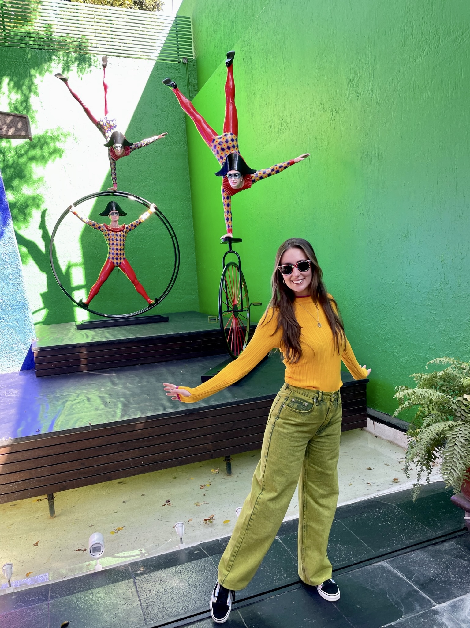 Susie standing in front of a saturated green courtyard wall